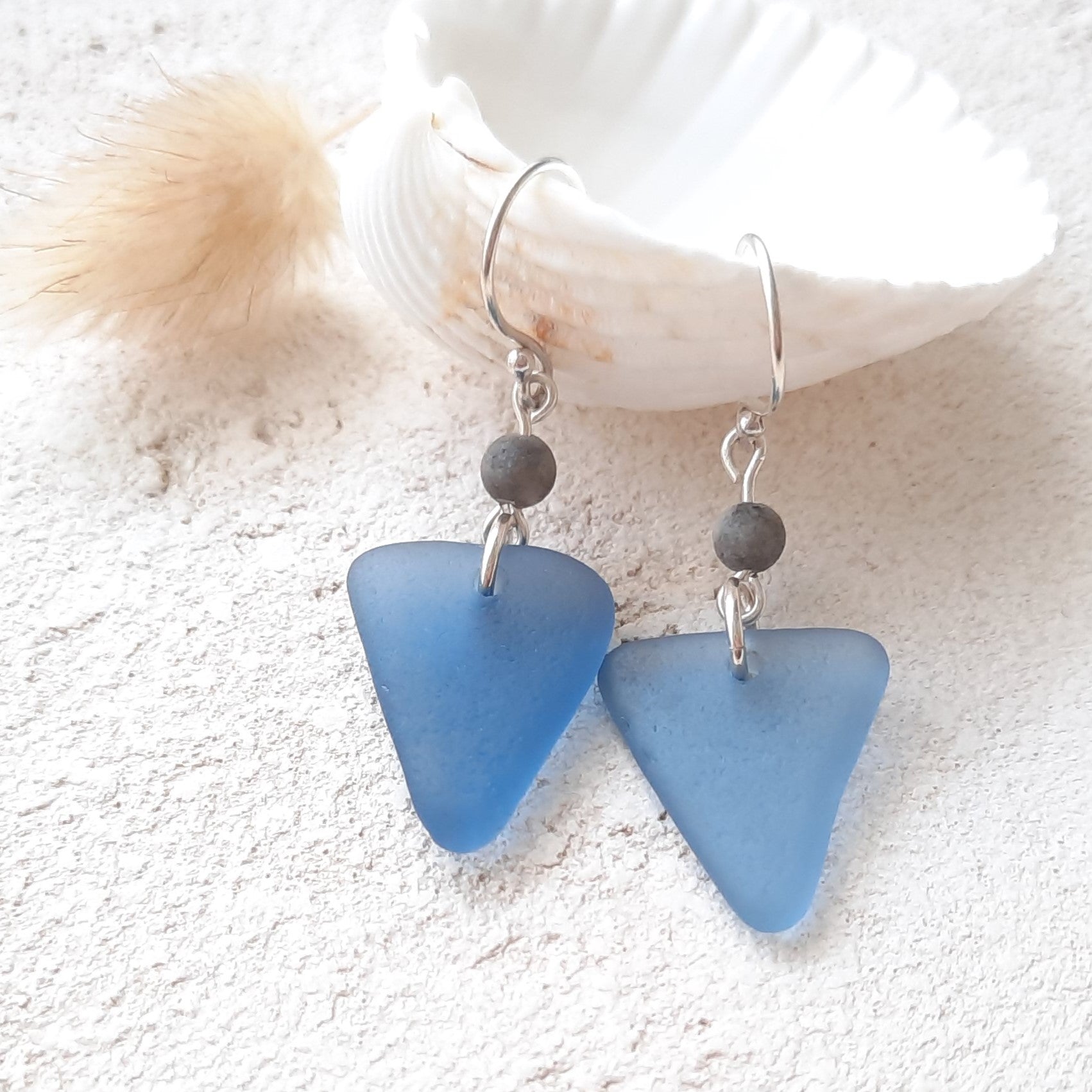 Blue triangle-shaped sea glass earrings with black amazonite beads on a textured white surface