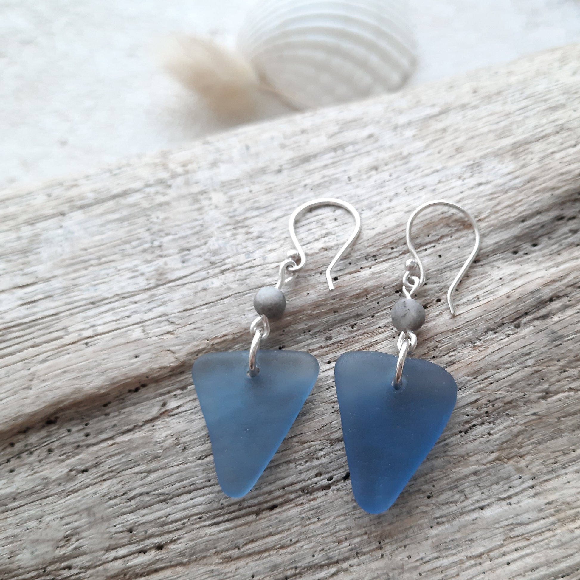 Blue triangle genuine sea glass earrings with silver hooks on a wooden surface