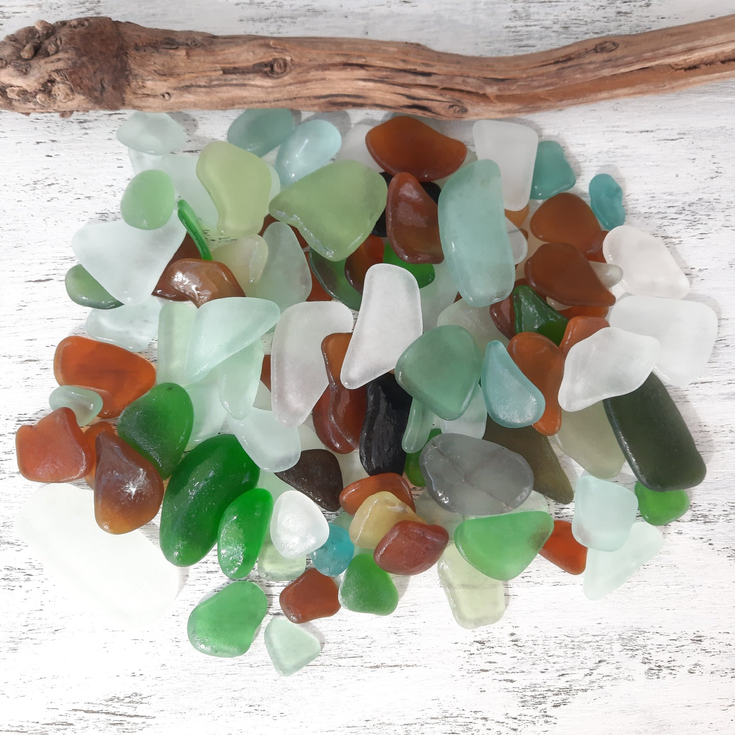 Assorted colored sea glass pieces on a white wooden surface with a piece of driftwood.
