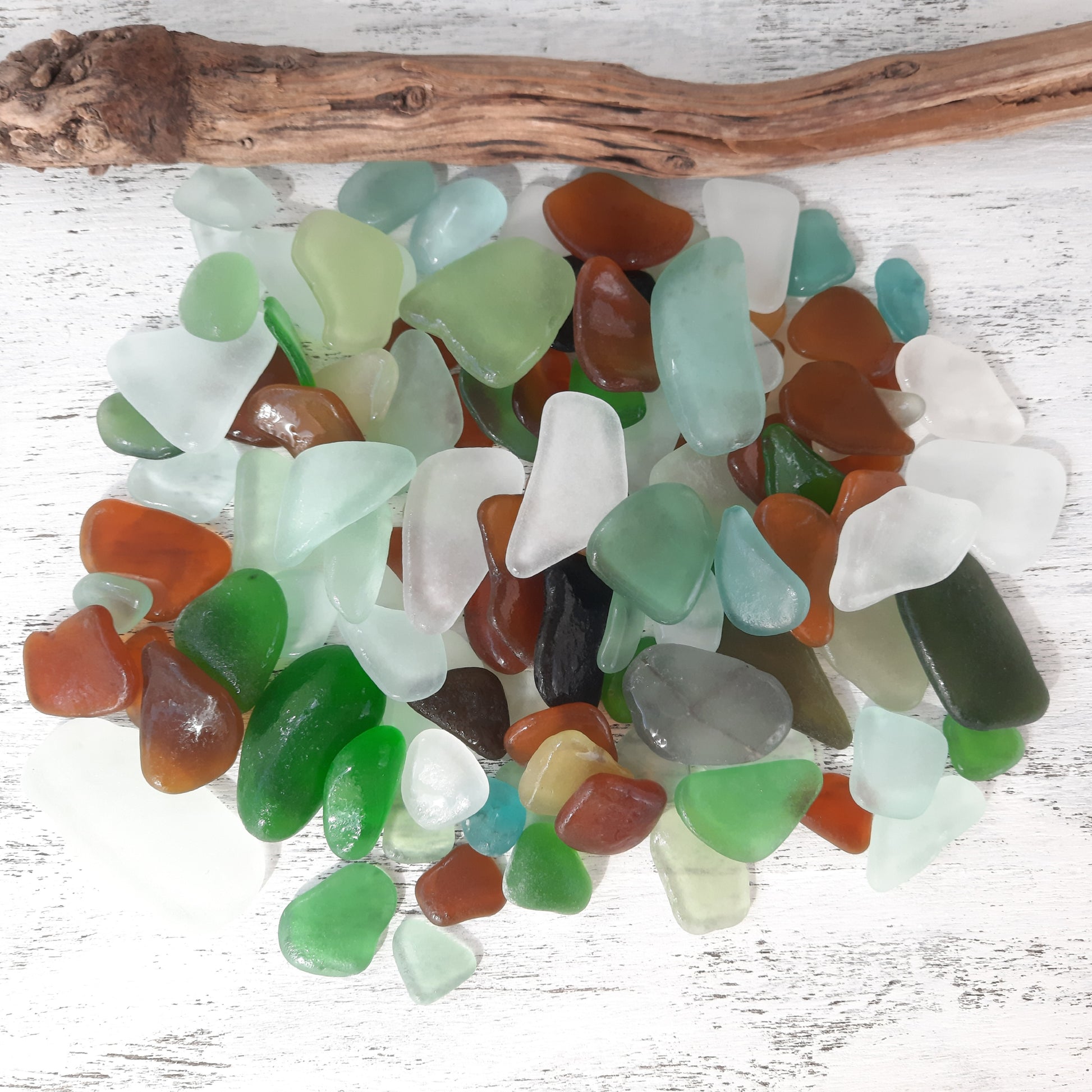 Assorted colored sea glass pieces on a white wooden surface with a piece of driftwood.