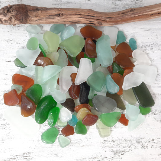 Assorted colored sea glass pieces on a white wooden surface with a piece of driftwood.