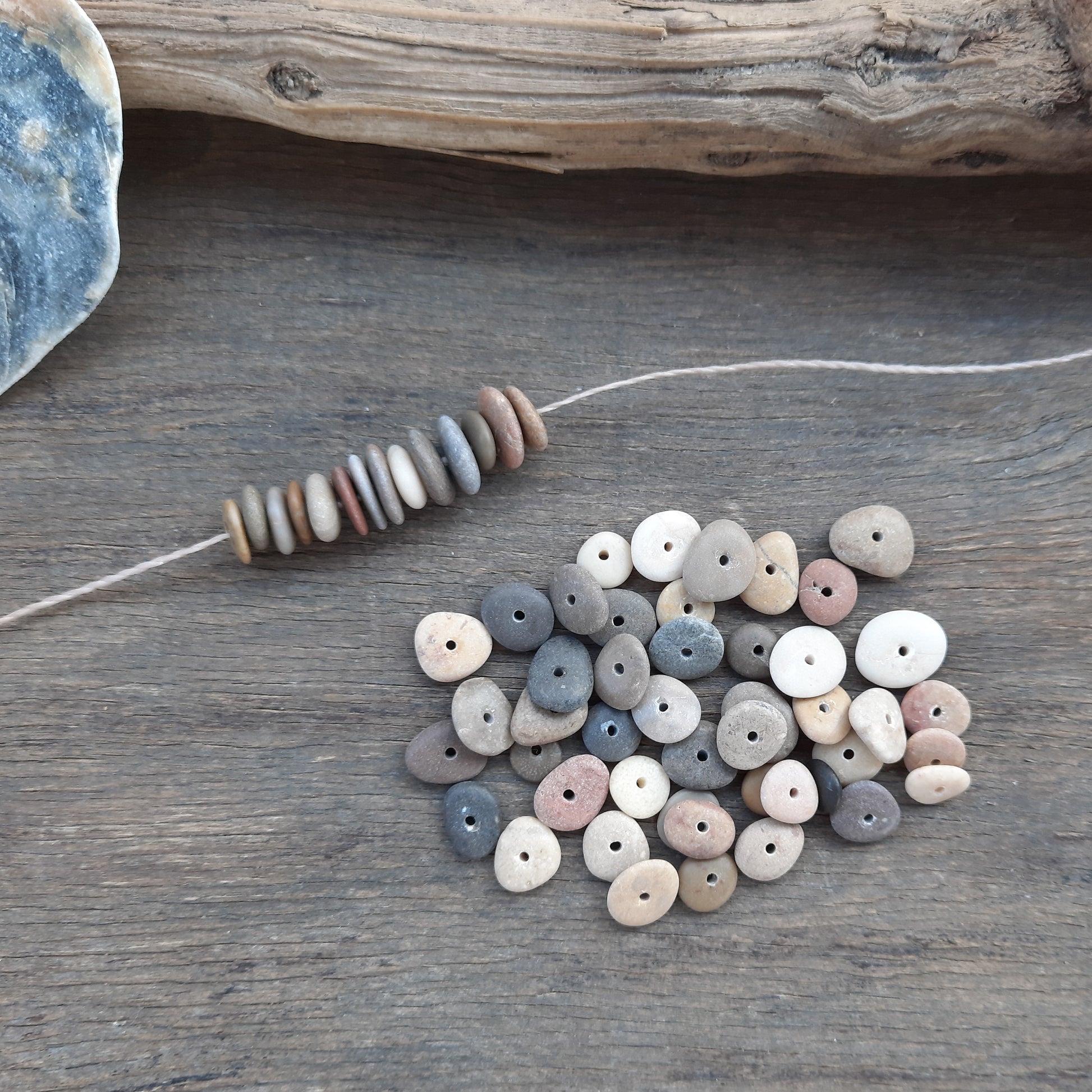 Set of natural-colored beach pebble beads on a wooden surface with a piece of driftwood.