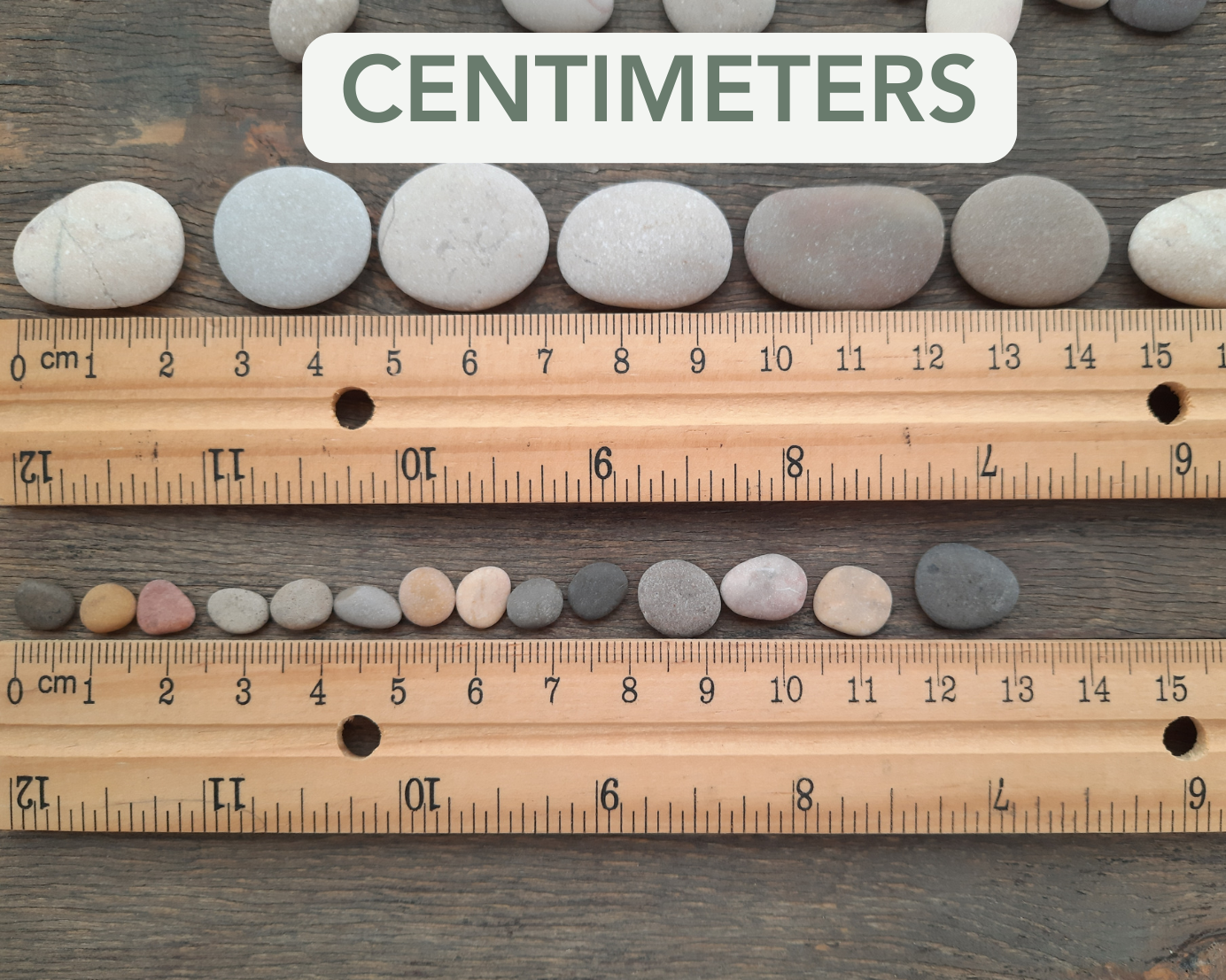 Rocks arranged next to a wooden ruler with centimeter markings on a wooden surface.