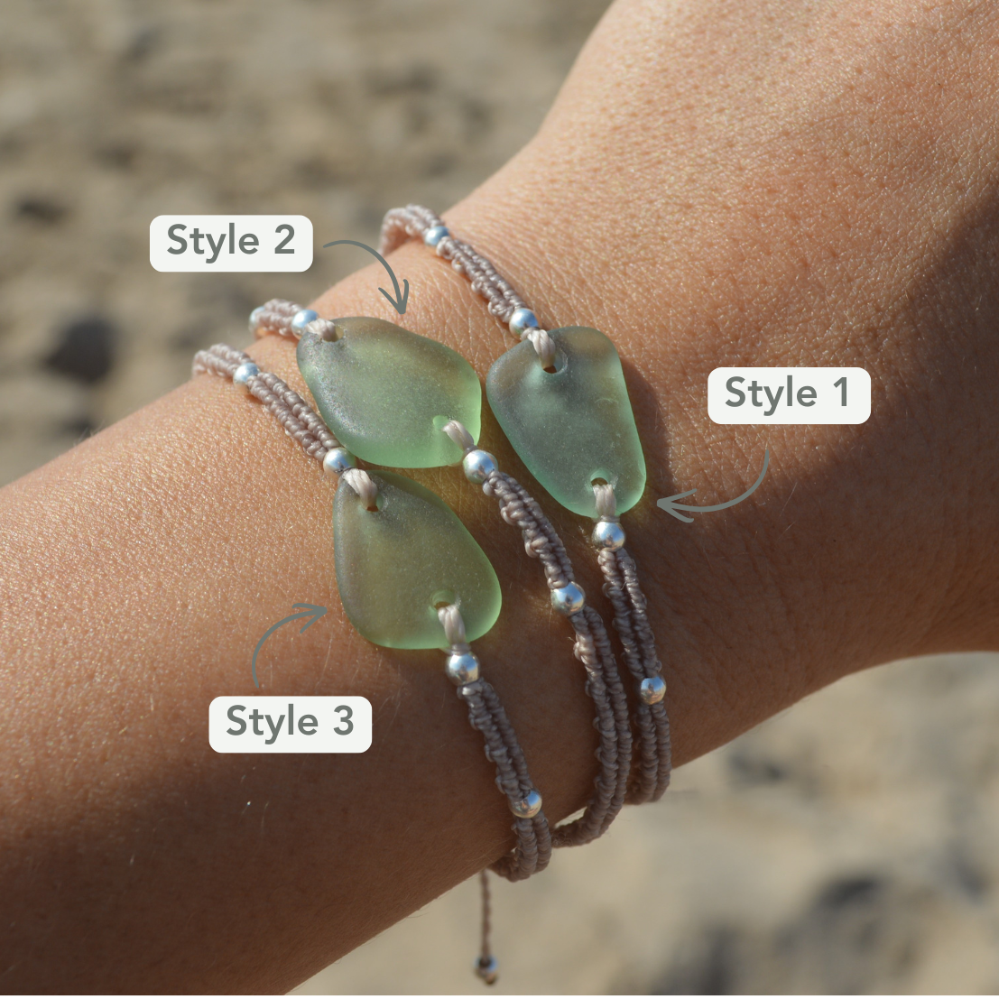 Three different styles of beach-style bracelets with seafoam green sea glass  and silver beads on beige cord, shown worn on a person's wrist against a sandy beach background.