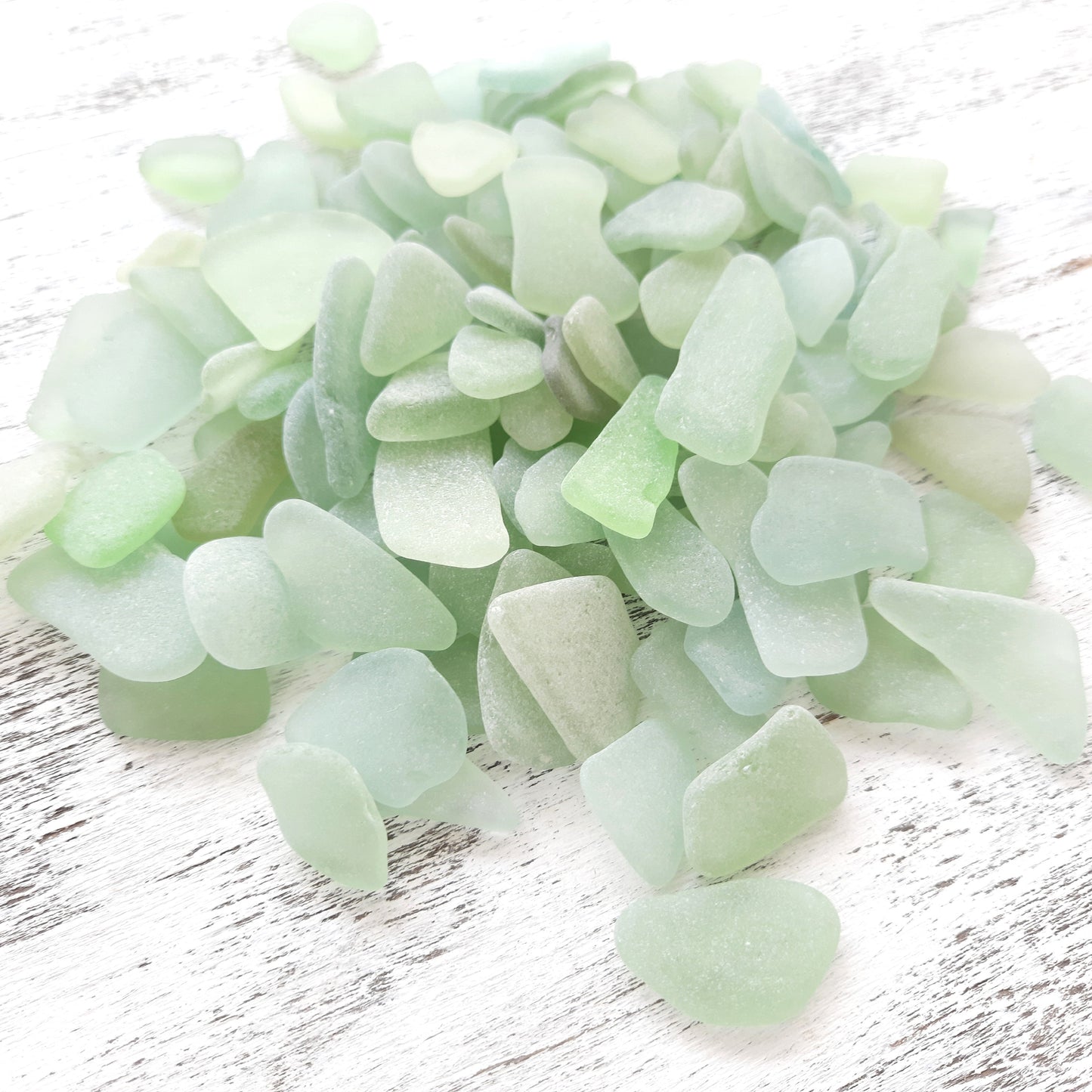 Collection of light green sea glass pieces on a white wooden surface